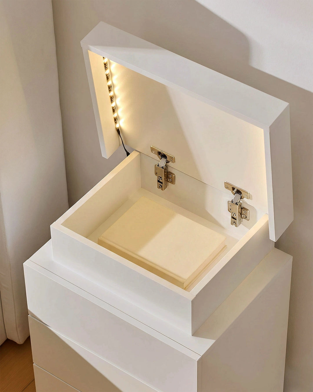 The hidden top storage lid of the white bedside table open with internal LED light on.