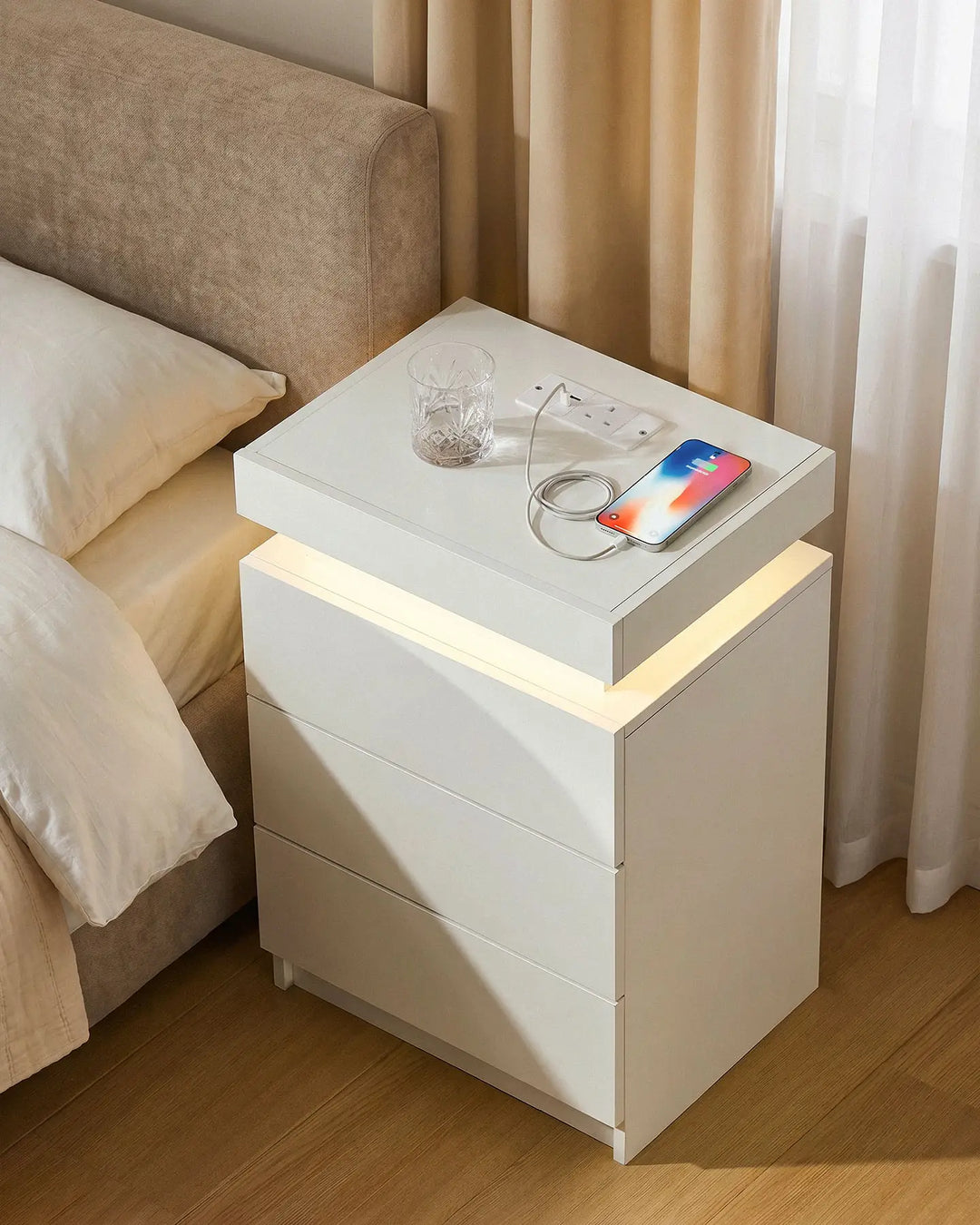Overhead view of the white bedside table with a phone and glass, showing the ambient glow.