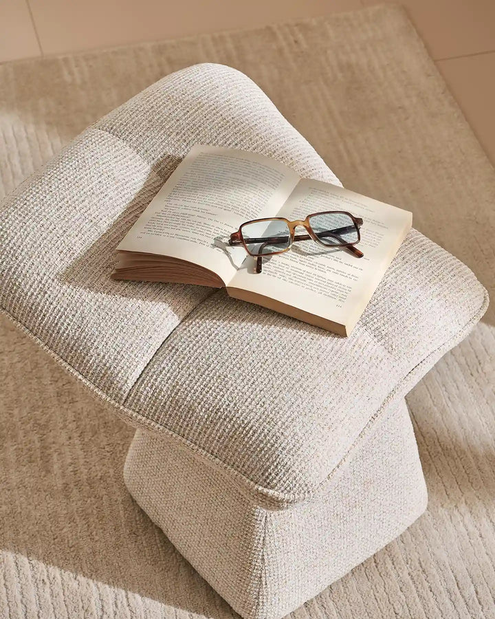 Liora beige swivel vanity stool styled with an open book and glasses on its softly padded seat, highlighting its comfortable design and textured upholstery