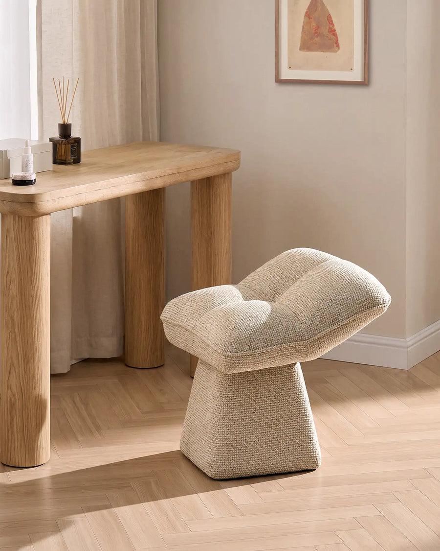 Liora beige swivel vanity stool styled beside a wooden console table in a warm neutral bedroom, featuring a softly padded seat and sculptural pedestal base