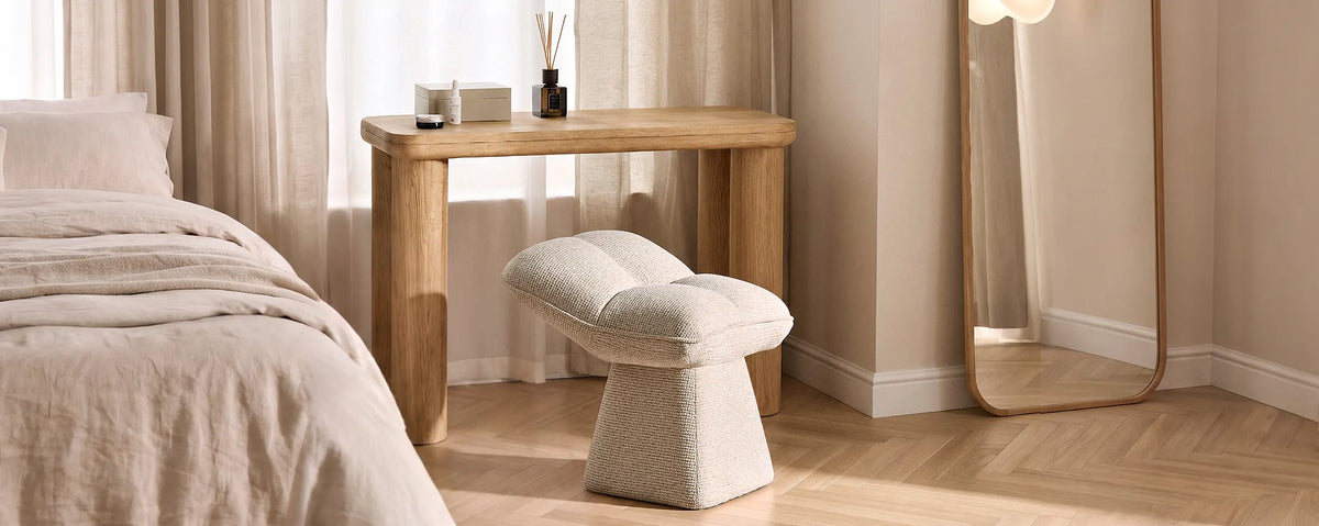 Liora beige swivel vanity stool positioned in a warm neutral bedroom beside a wooden dressing area, with soft bedding and natural textures