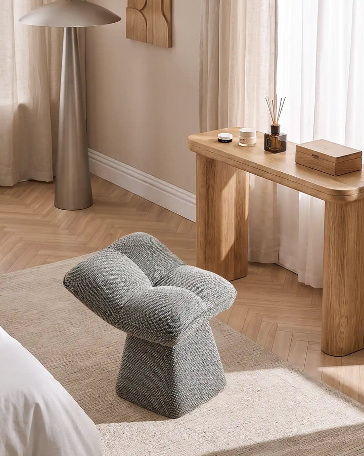 Liora grey swivel vanity stool placed beside a wooden dressing table in a bright bedroom, complementing the neutral interior and natural wood flooring