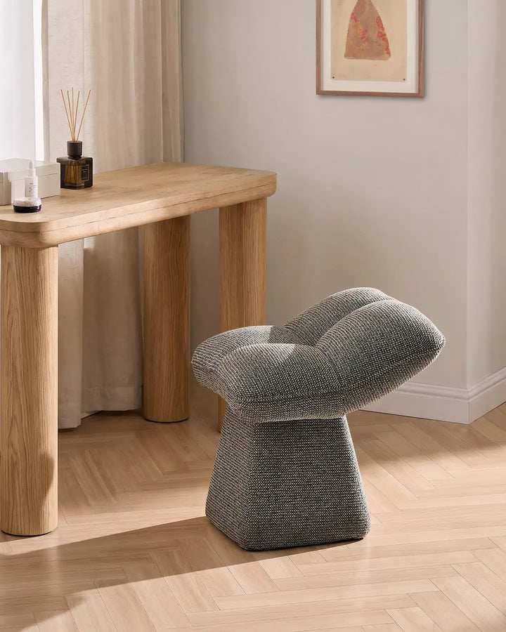 Liora grey swivel vanity stool styled beside a wooden console table in a warm neutral bedroom, featuring a softly padded seat and sculptural pedestal base