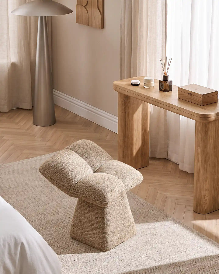 Liora khaki swivel vanity stool placed beside a wooden dressing table in a bright bedroom, complementing the neutral interior and natural wood flooring