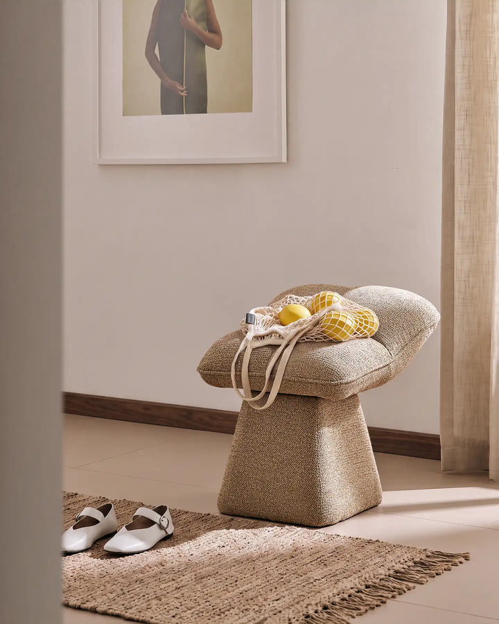 Liora khaki swivel vanity stool used as an entryway seat in a warm hallway, with a bag of lemons placed on the cushioned seat