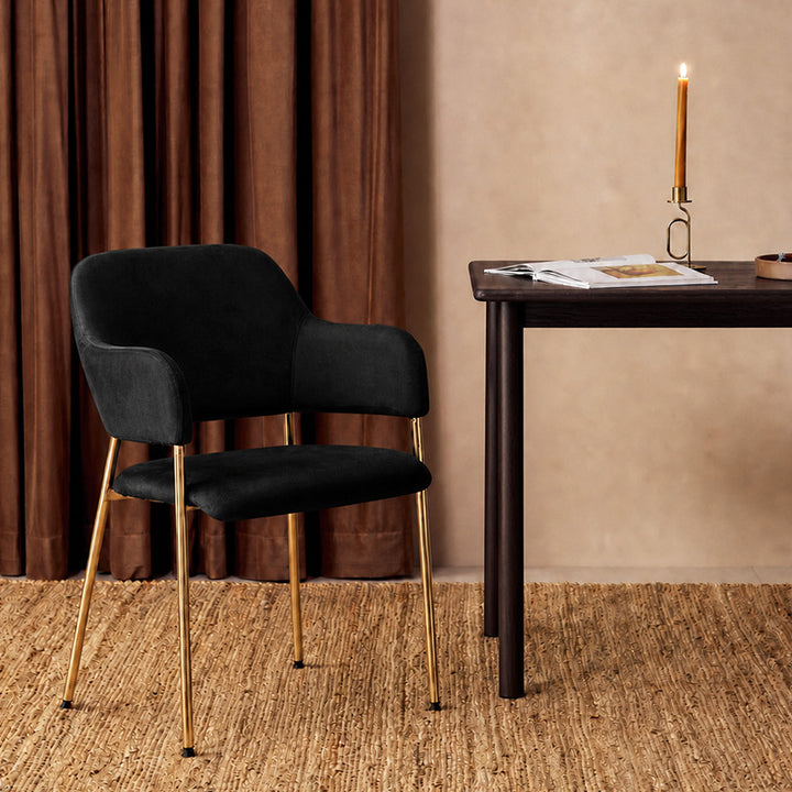 Lukka Velvet Dining Chair with gold colour metal legs, beside a table
