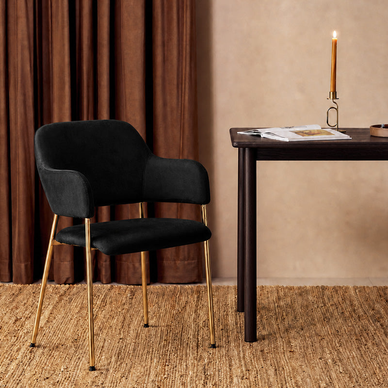 Lukka Velvet Dining Chair with gold colour metal legs, beside a table