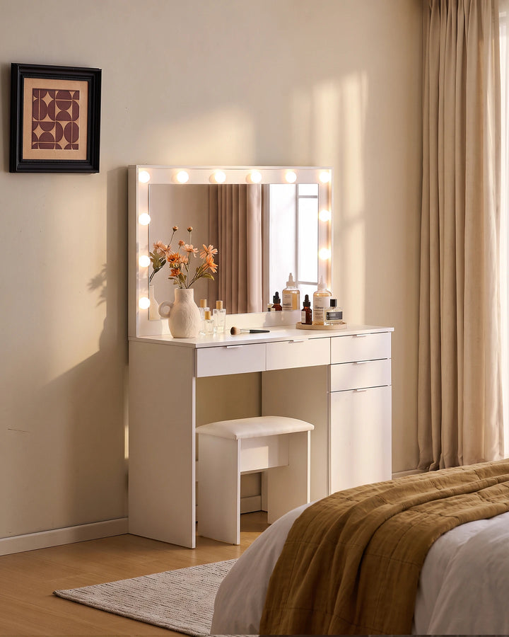 Lunea white dressing table set with illuminated mirror and matching stool styled beside a bed with neutral bedding and warm beige curtains.