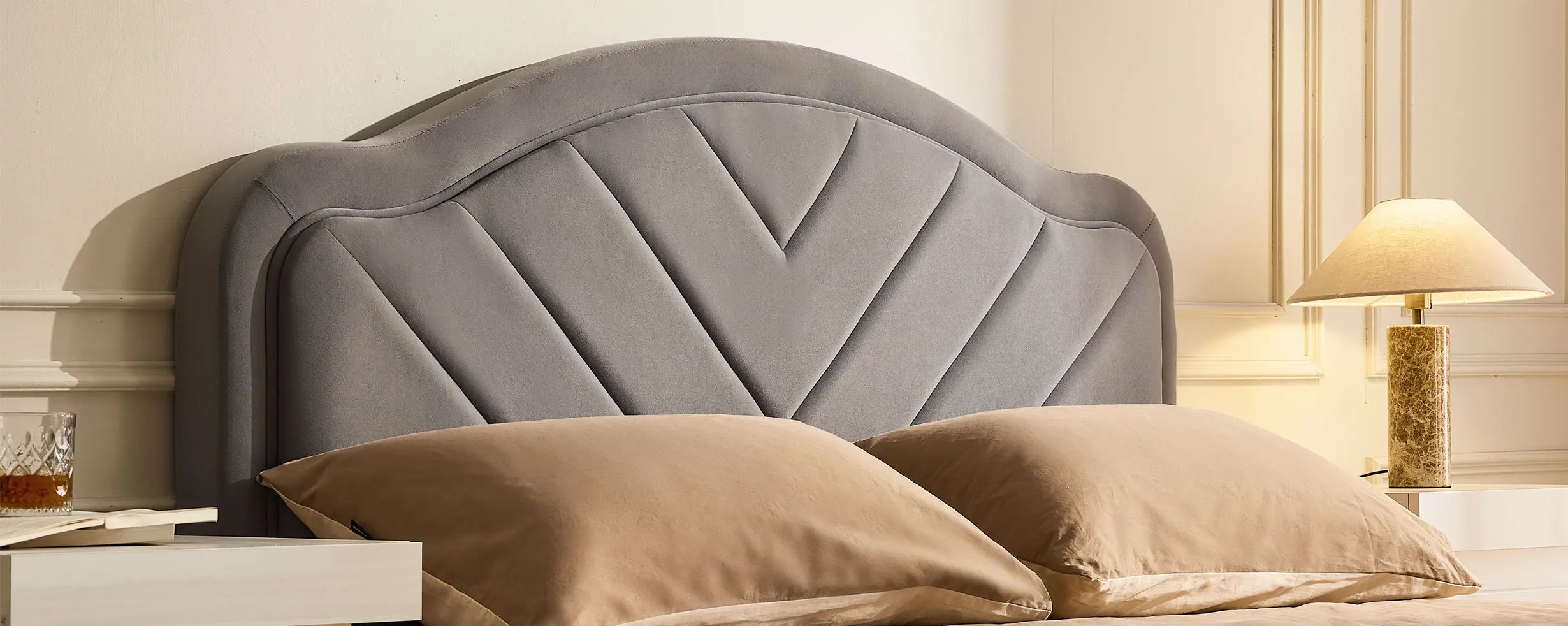 Close-up of grey velvet upholstered headboard on double bed frame with soft texture and V-stitch detail
