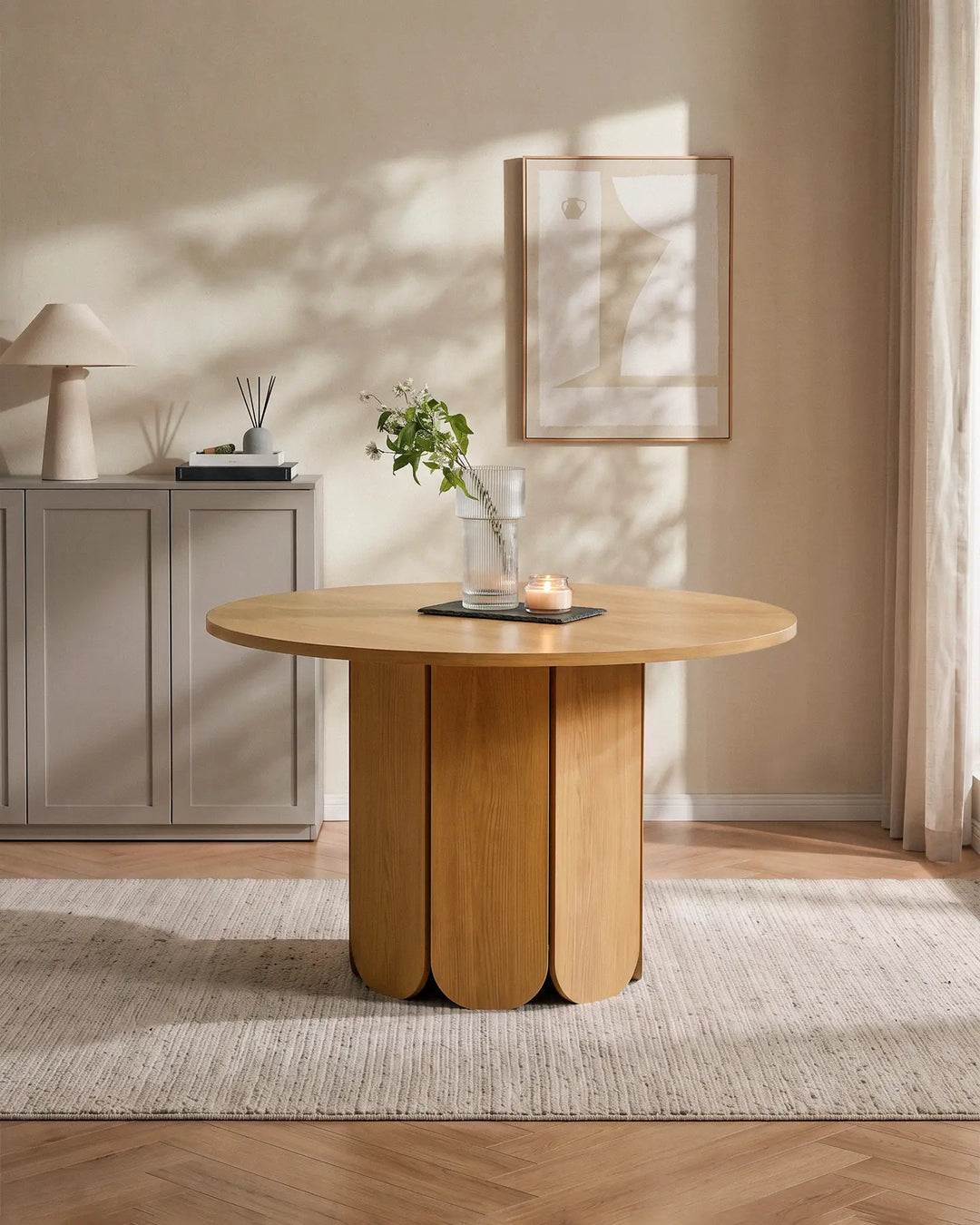 Nara round dining table with a sculptural pedestal base in a bright, neutral dining room, styled with a vase of greenery