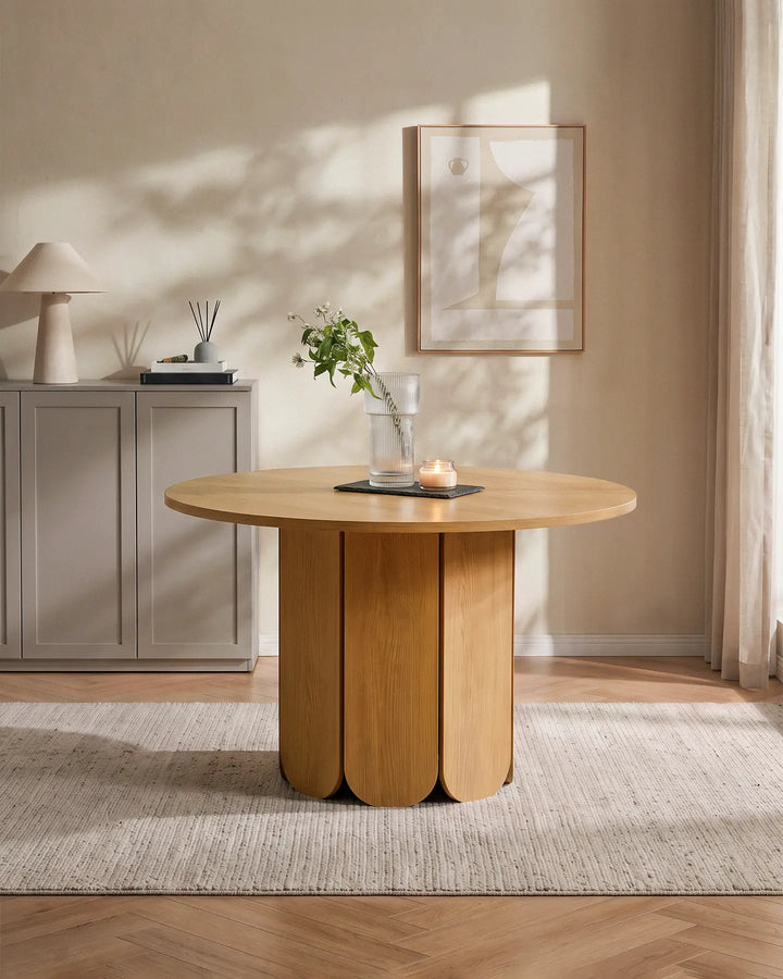 Nara round dining table with a sculptural pedestal base in a bright, neutral dining room, styled with a vase of greenery